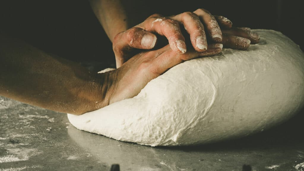 Pétrissage de la pâte à pizza par un pizzaiolo, illustrant le savoir-faire artisanal et l'importance de cette étape.