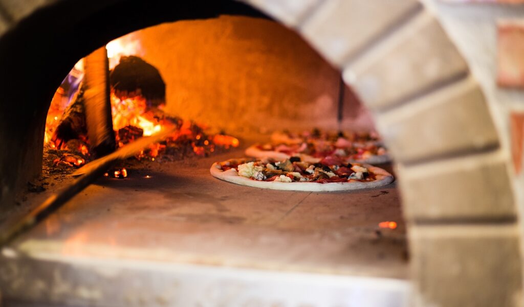 Pizzas napolitaines cuisant dans un four à bois traditionnel, avec des braises rouges et un feu vif.