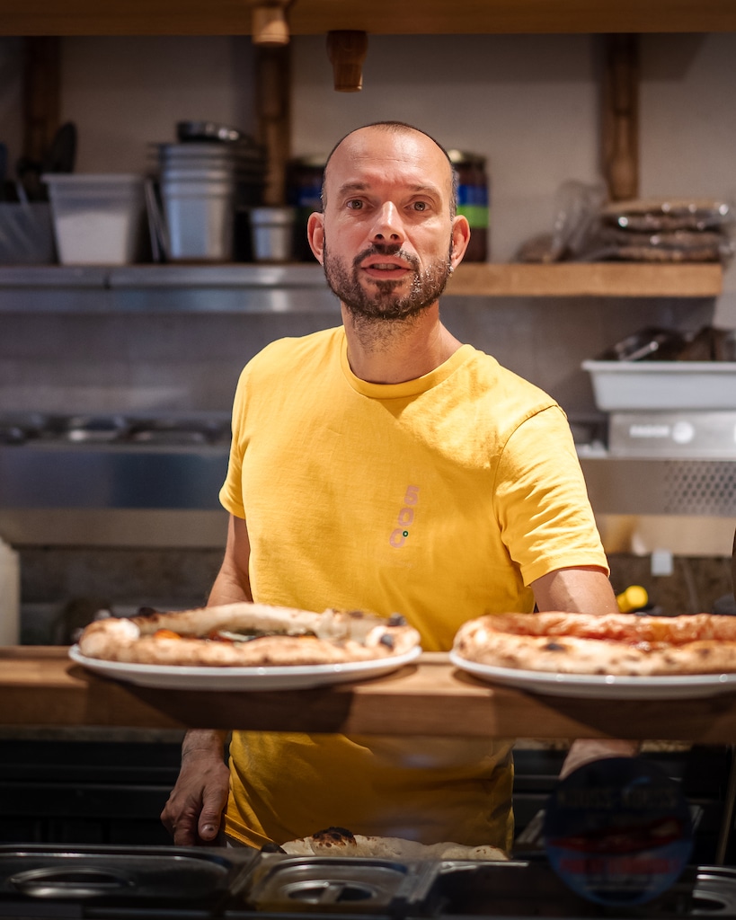 Olivier Poizat, formateur en pizza napolitaine, debout derrière un comptoir avec des pizzas artisanales à la pizzeria 500degrés